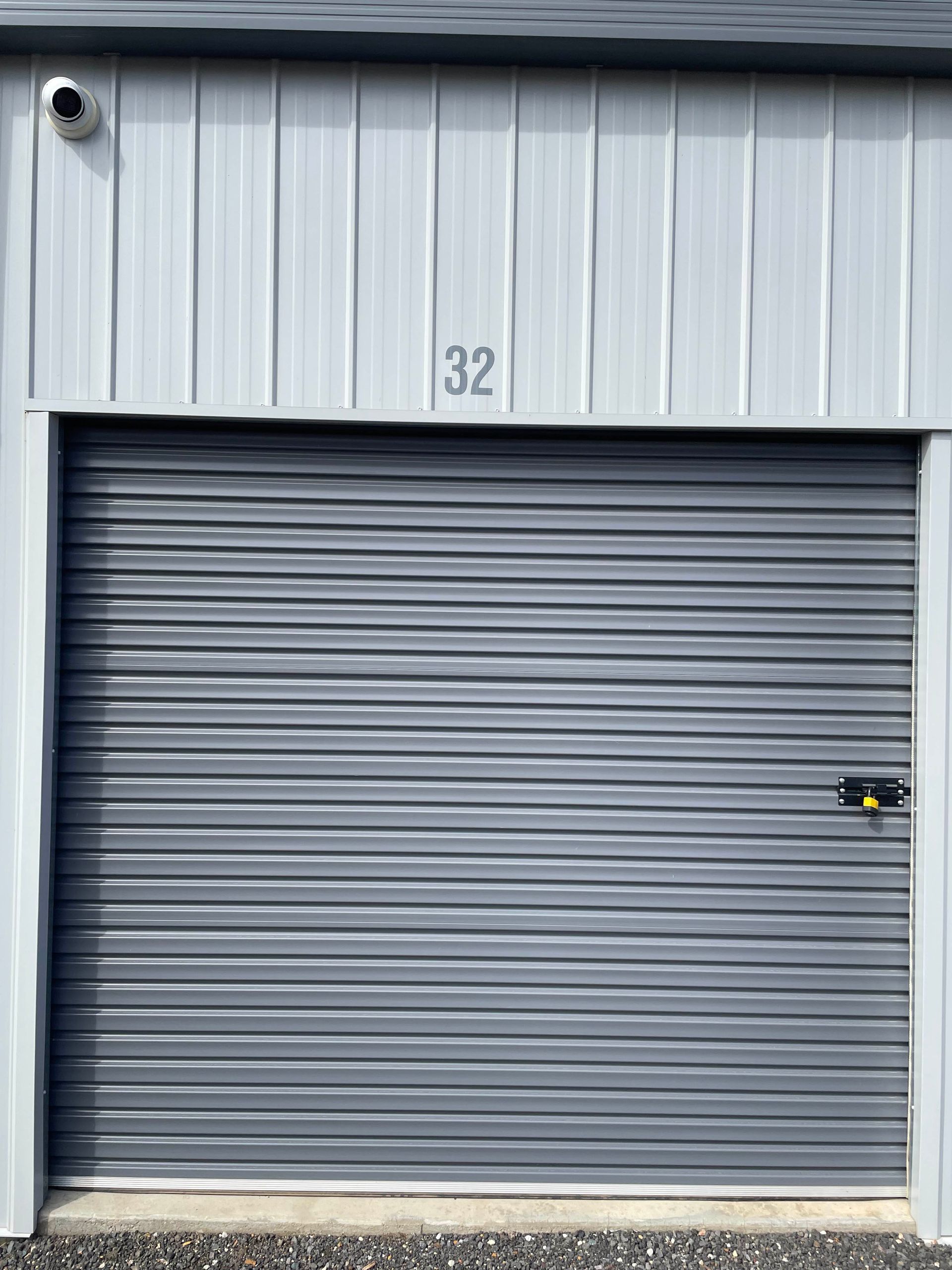 Gray metal roll-up door on a storage unit labeled 32 with a small lock on the right