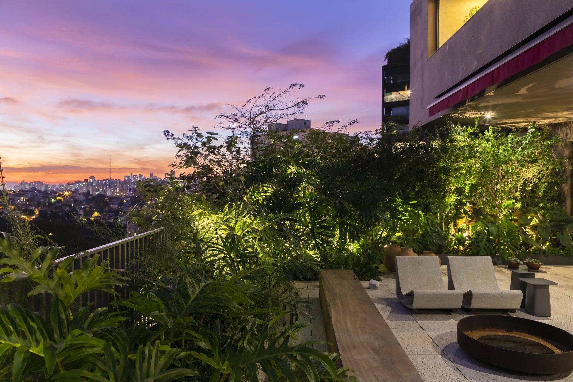 Um pátio com sofá e mesa em frente a um prédio ao pôr do sol.