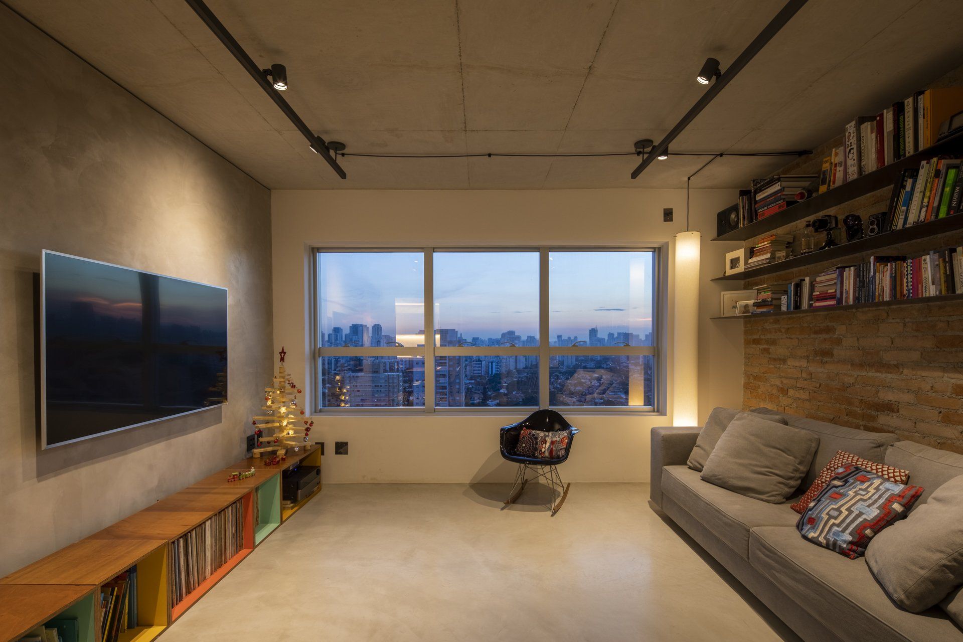 Uma sala com sofá, televisão, estante e grande janela.