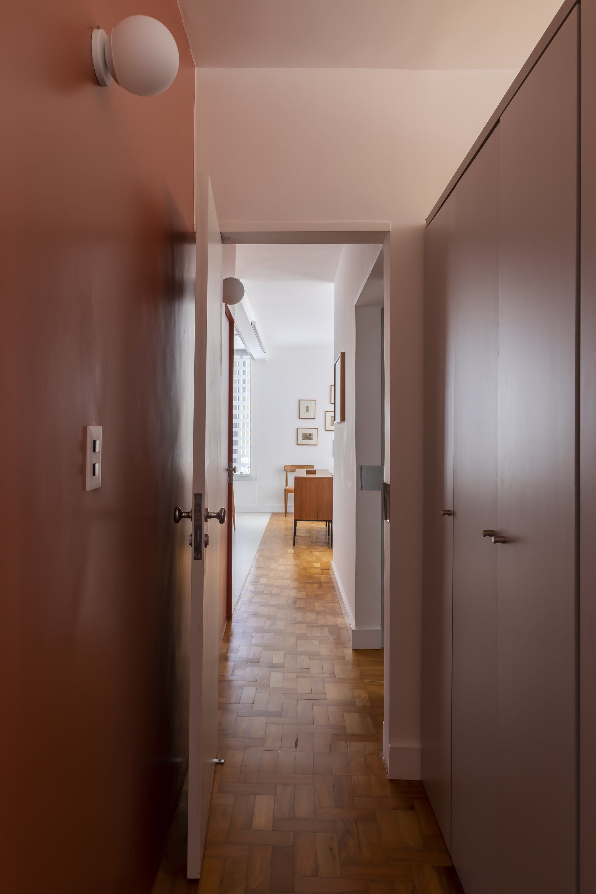 Um corredor com piso de madeira e uma parede vermelha que dá acesso a uma sala de estar.