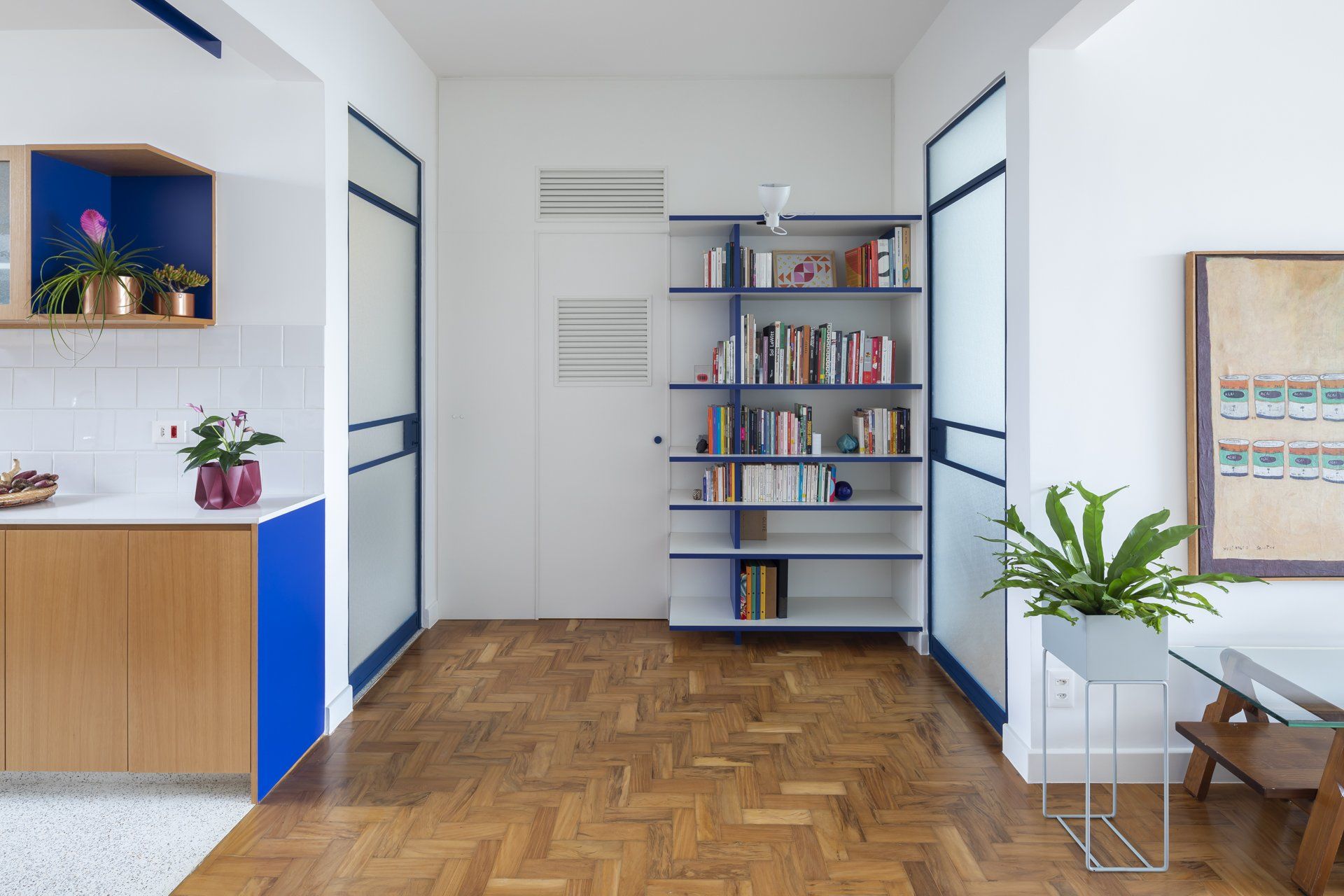 Uma sala com piso de madeira, uma estante e um quadro na parede.