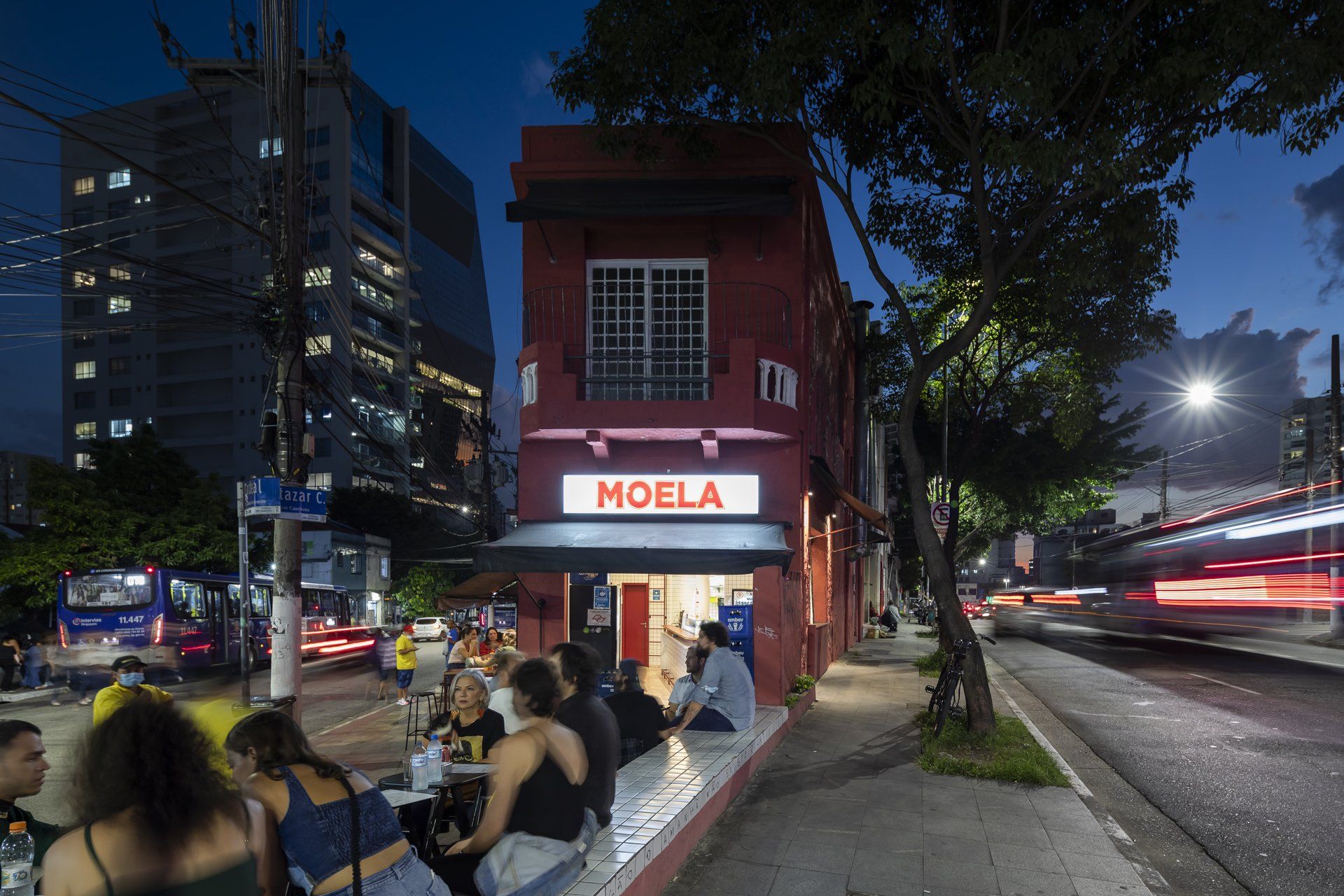 Um grupo de pessoas está sentado do lado de fora de um restaurante chamado noela
