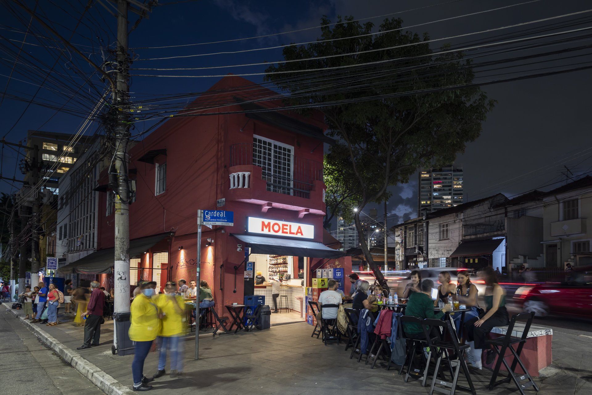 Um grupo de pessoas está sentado do lado de fora de um restaurante à noite.