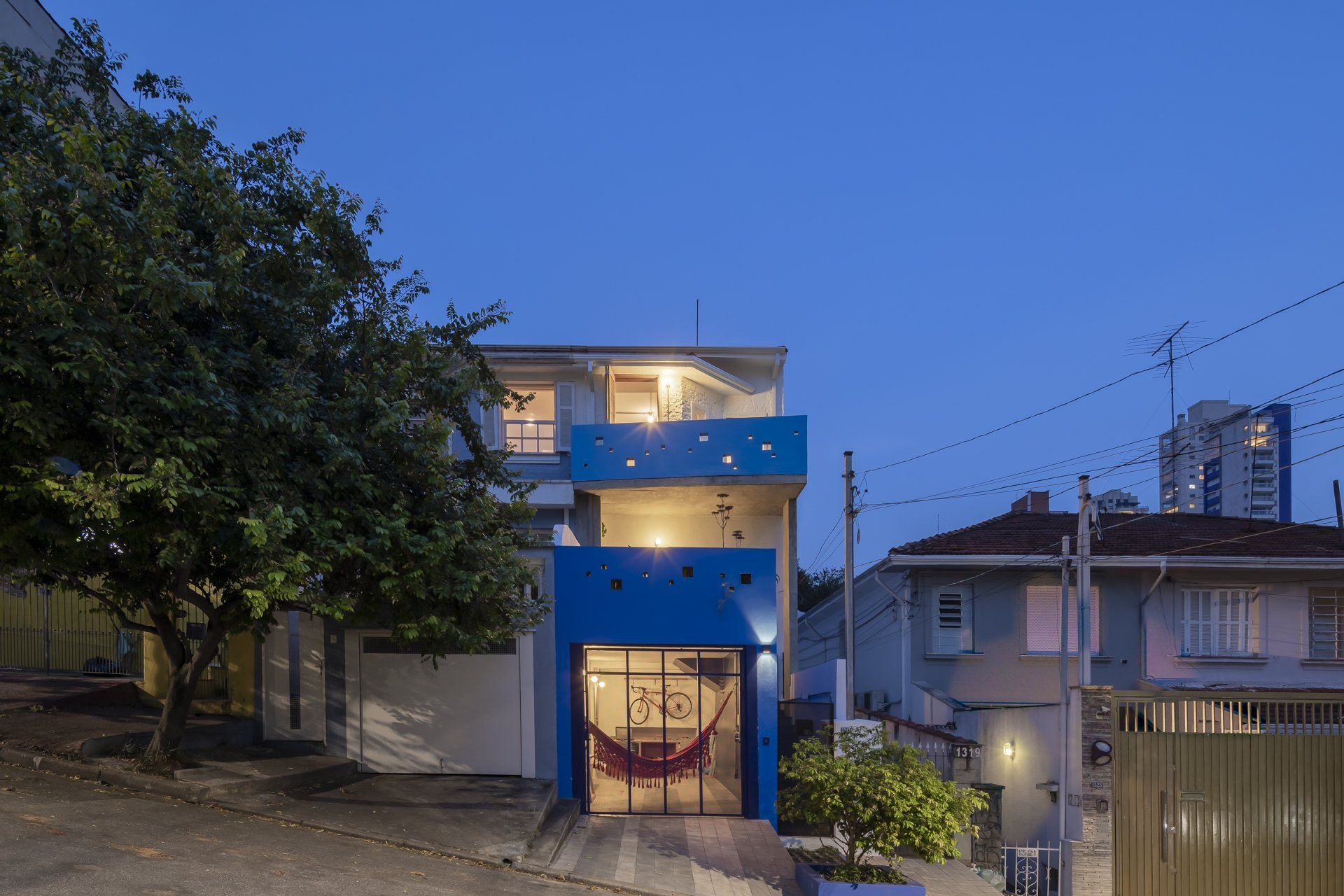Uma casa azul com uma rede na frente fica iluminada à noite.
