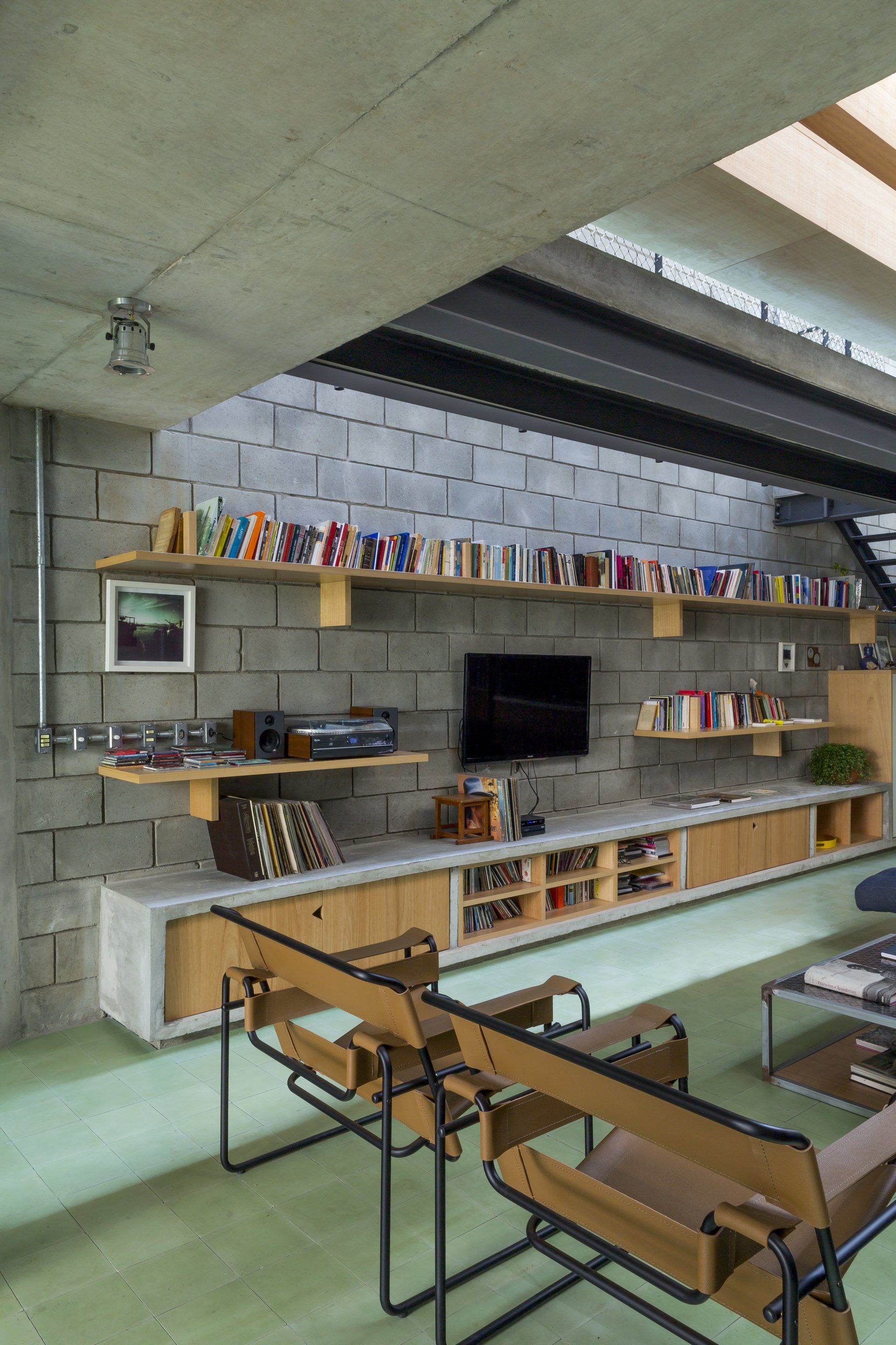 Uma sala com parede de tijolos, cadeiras, estantes e televisão.