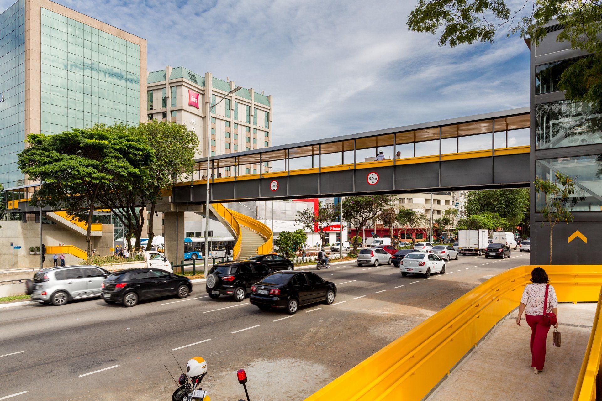Uma mulher está atravessando uma ponte sobre uma rua movimentada.