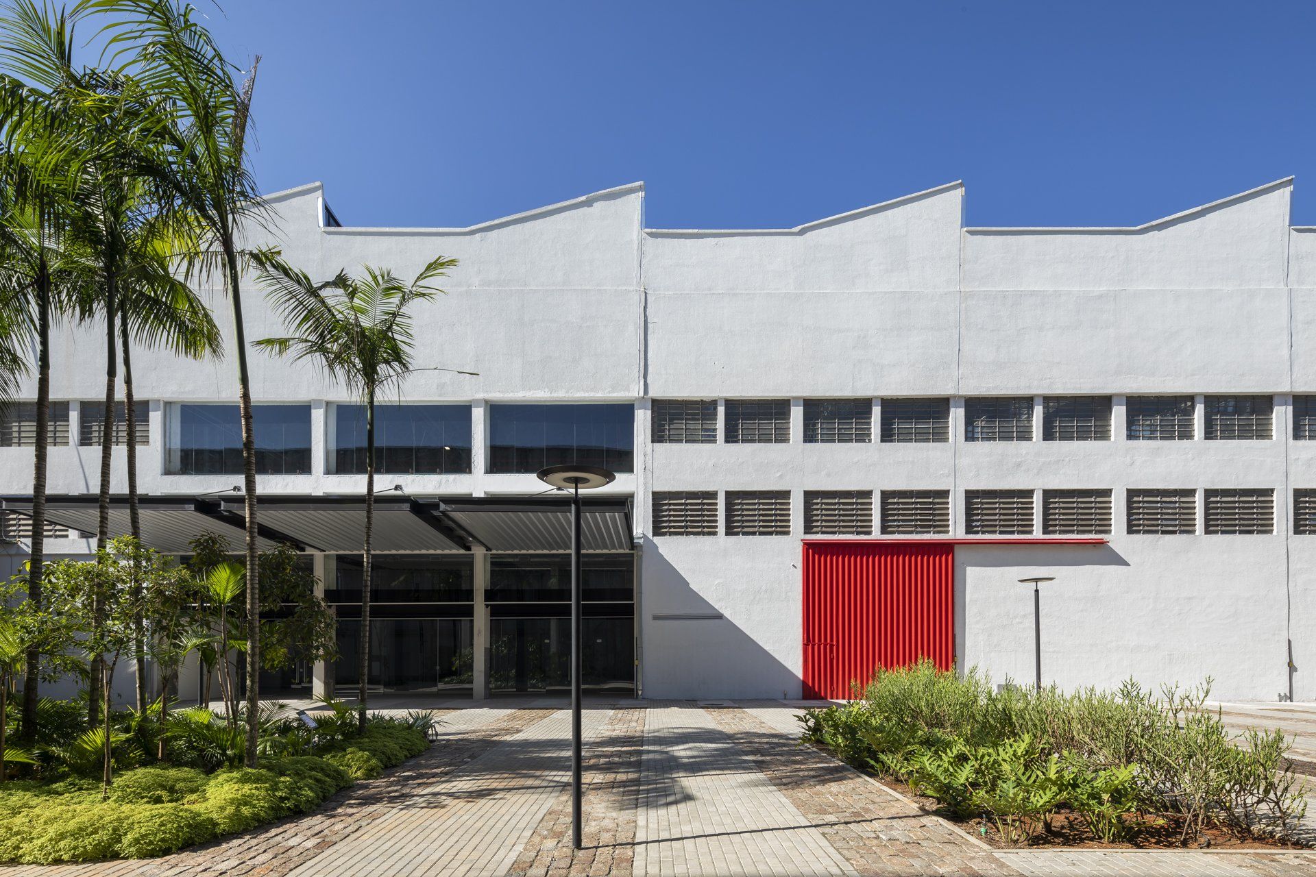 Um grande edifício branco com uma porta vermelha e palmeiras na frente.