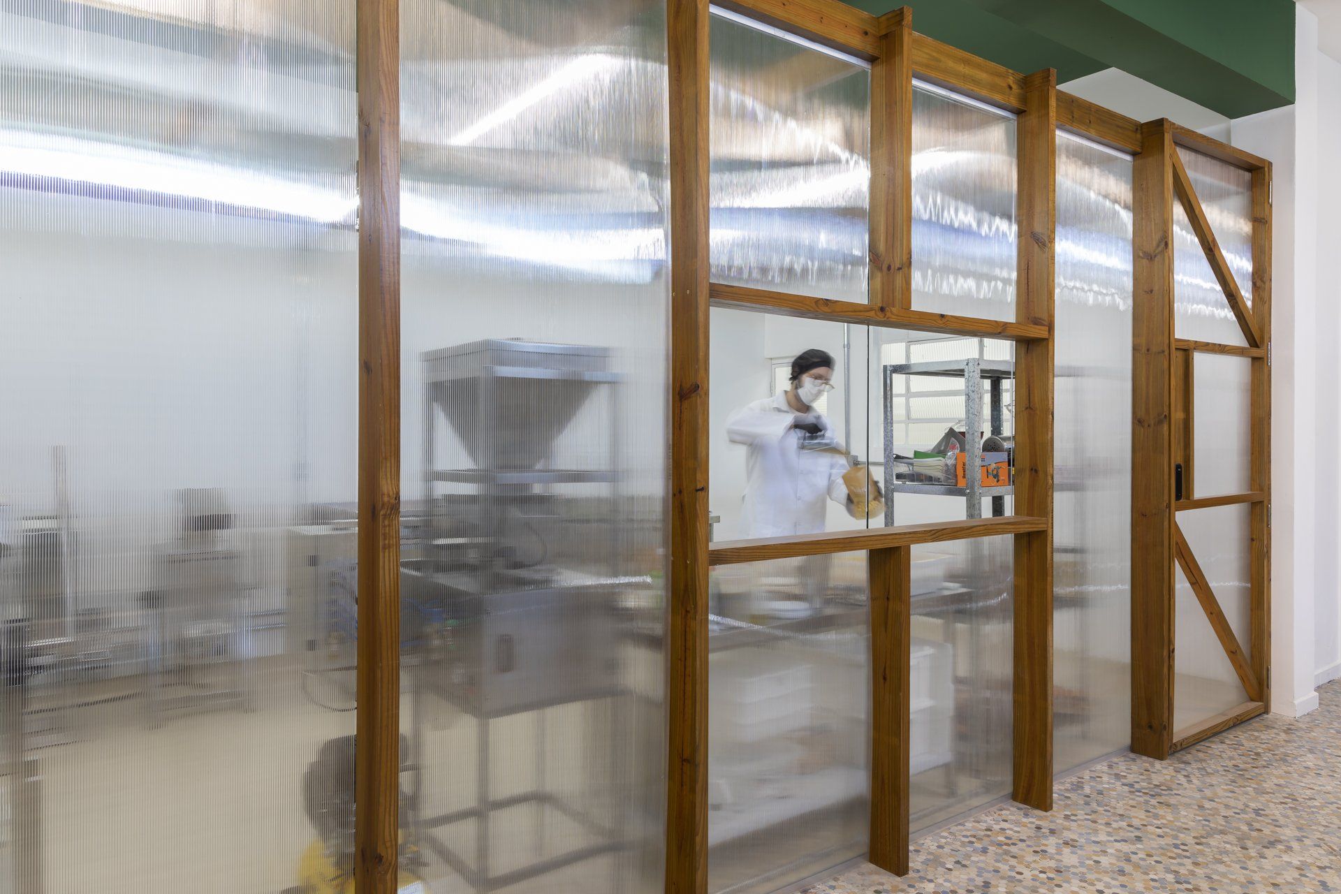 Um homem está parado em uma sala atrás de uma parede de plástico transparente.