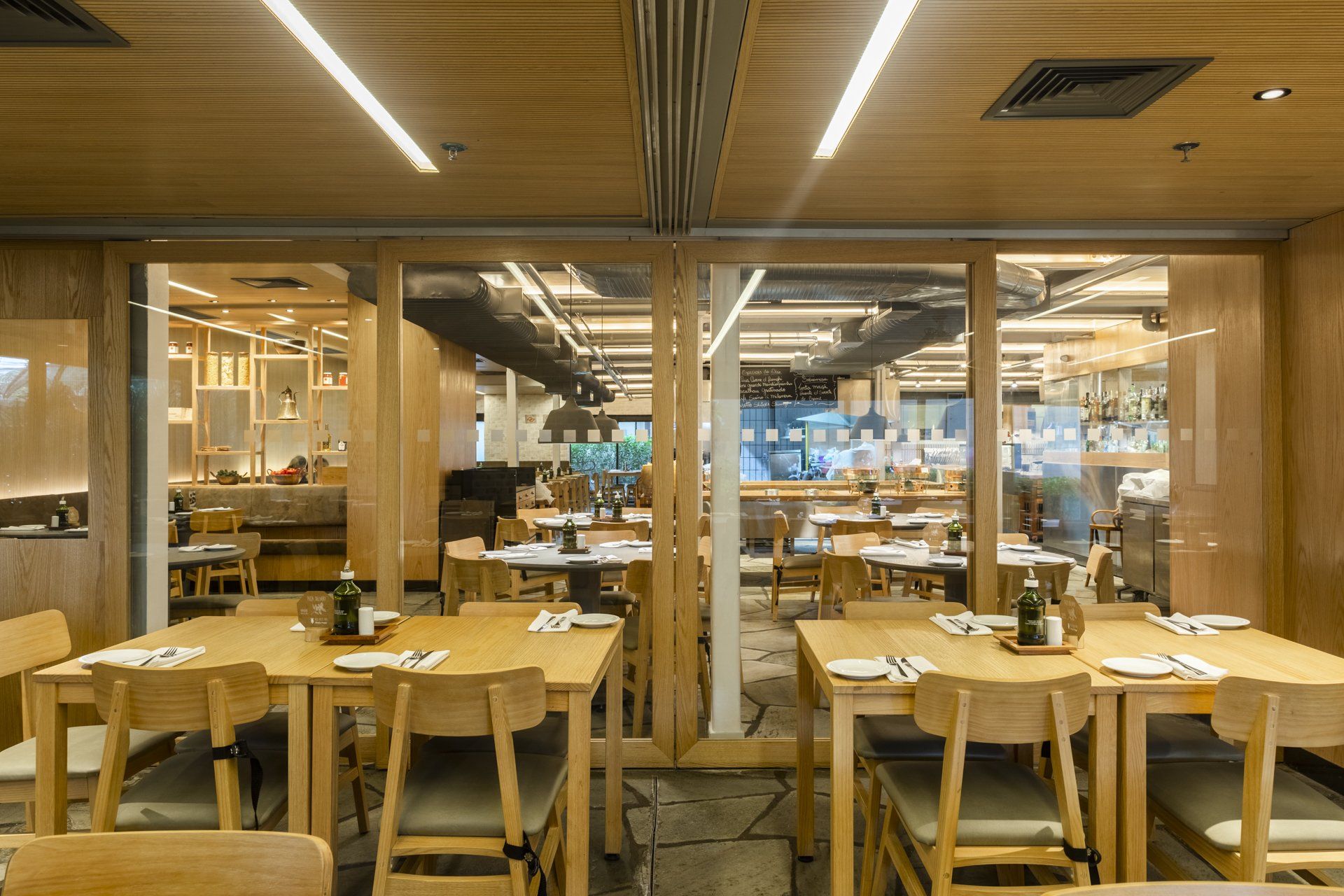 Um restaurante com mesas e cadeiras de madeira e parede de vidro.