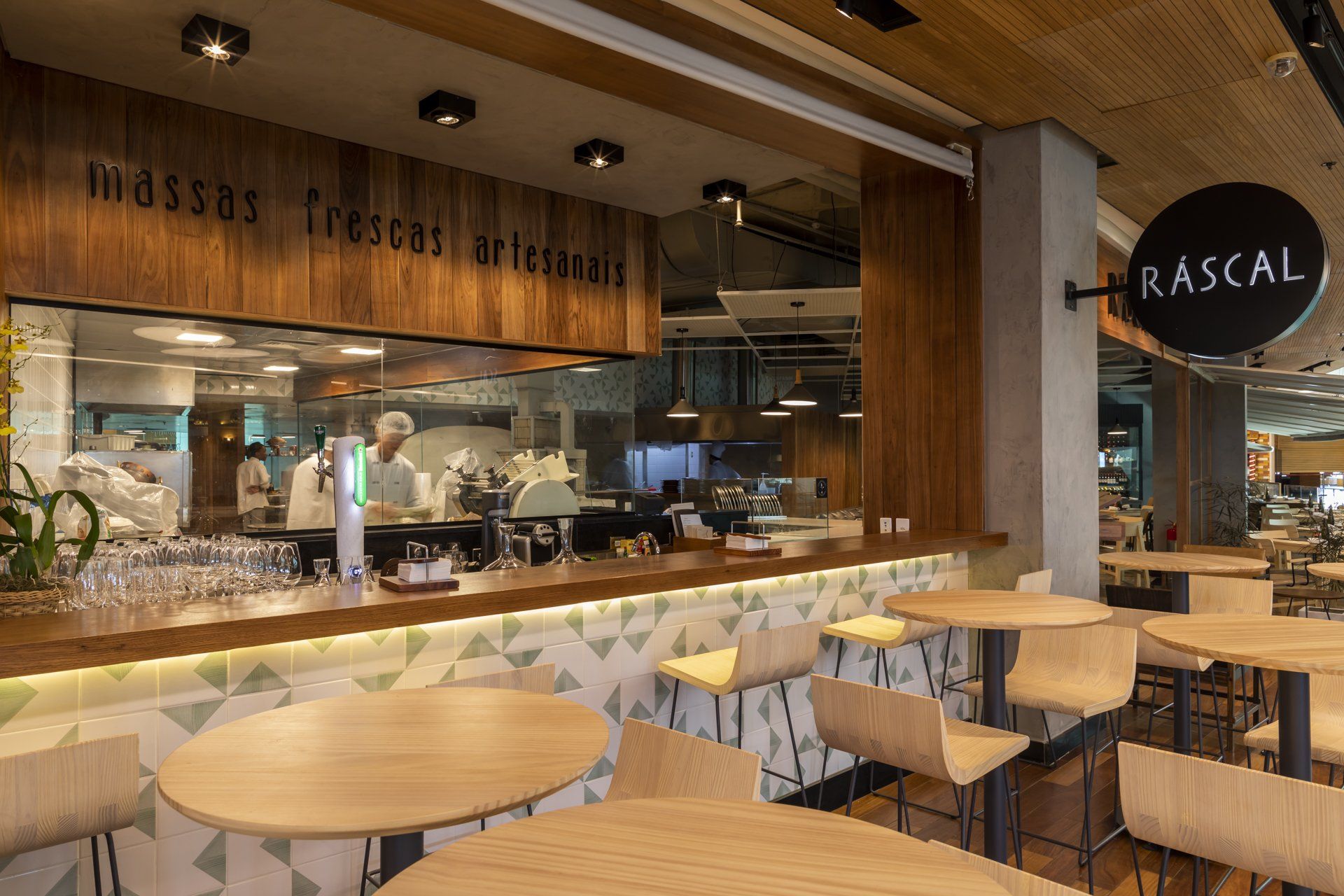 Um restaurante com mesas e cadeiras e uma cozinha ao fundo.