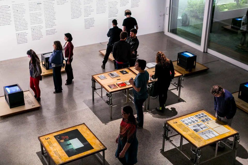 Um grupo de pessoas está em volta de mesas em um museu.