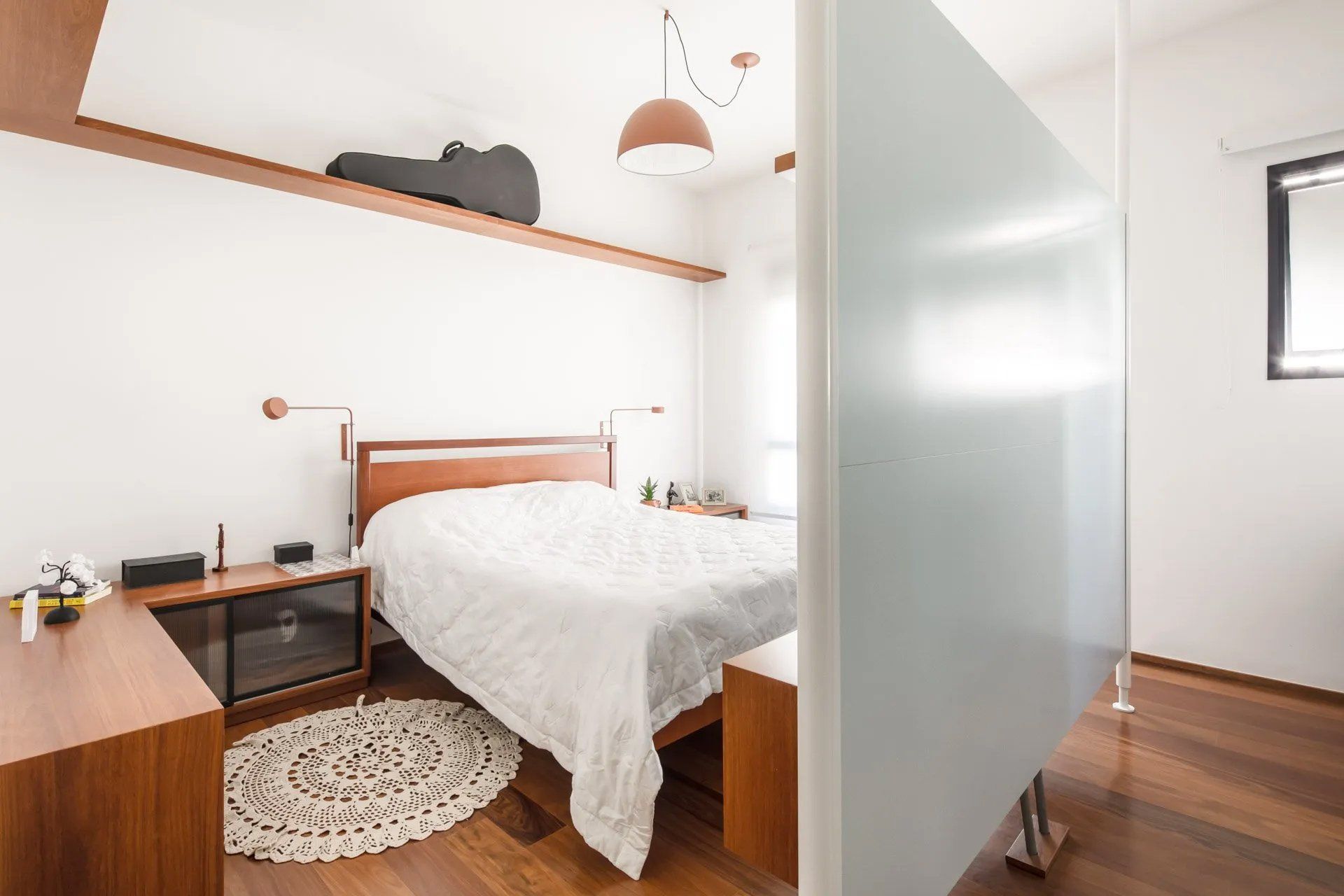 Um quarto com cama, mesa de cabeceira e parede de vidro.
