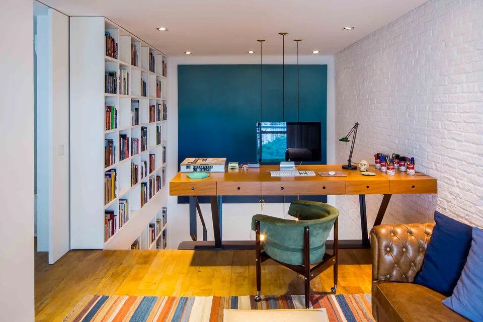 Uma sala de estar com escrivaninha, cadeira, sofá e estante.