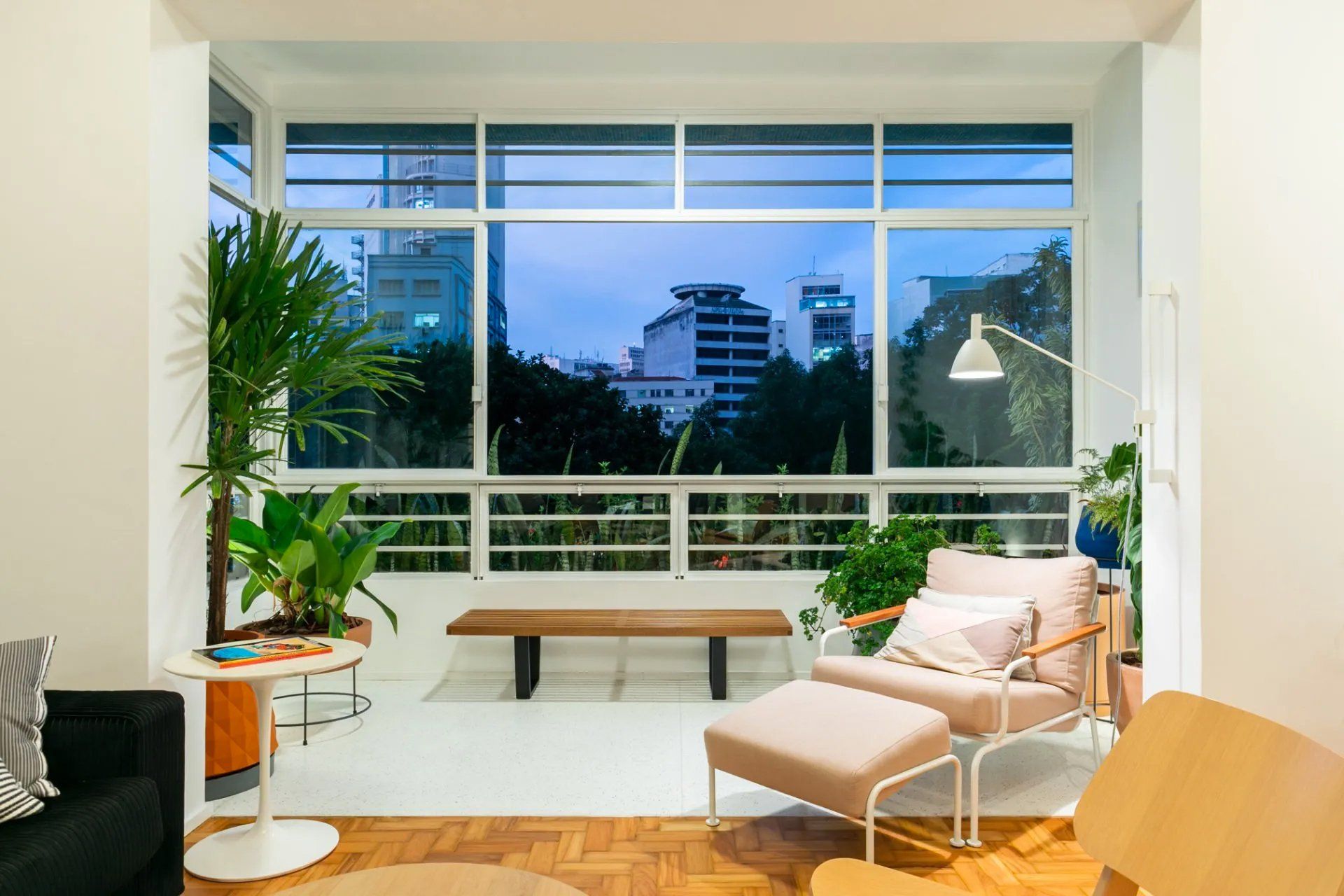 Uma sala de estar com sofá, cadeira, pufe e uma grande janela.