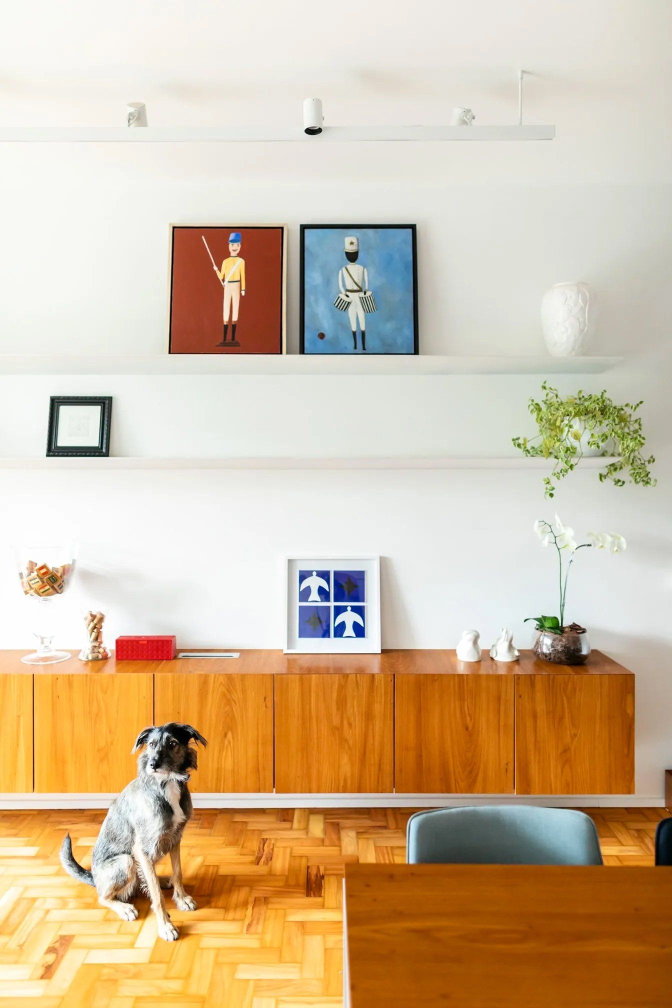 Um cachorro está sentado no chão de uma sala ao lado de uma mesa.