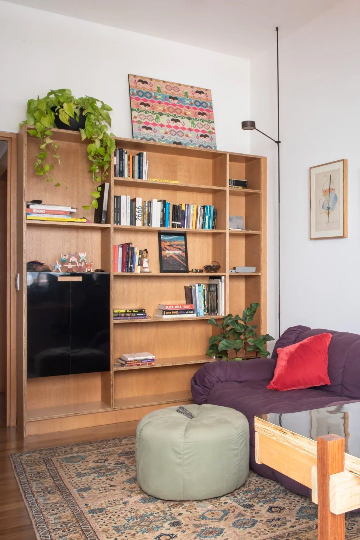 Uma sala com sofá, estante, pufe e tapete.