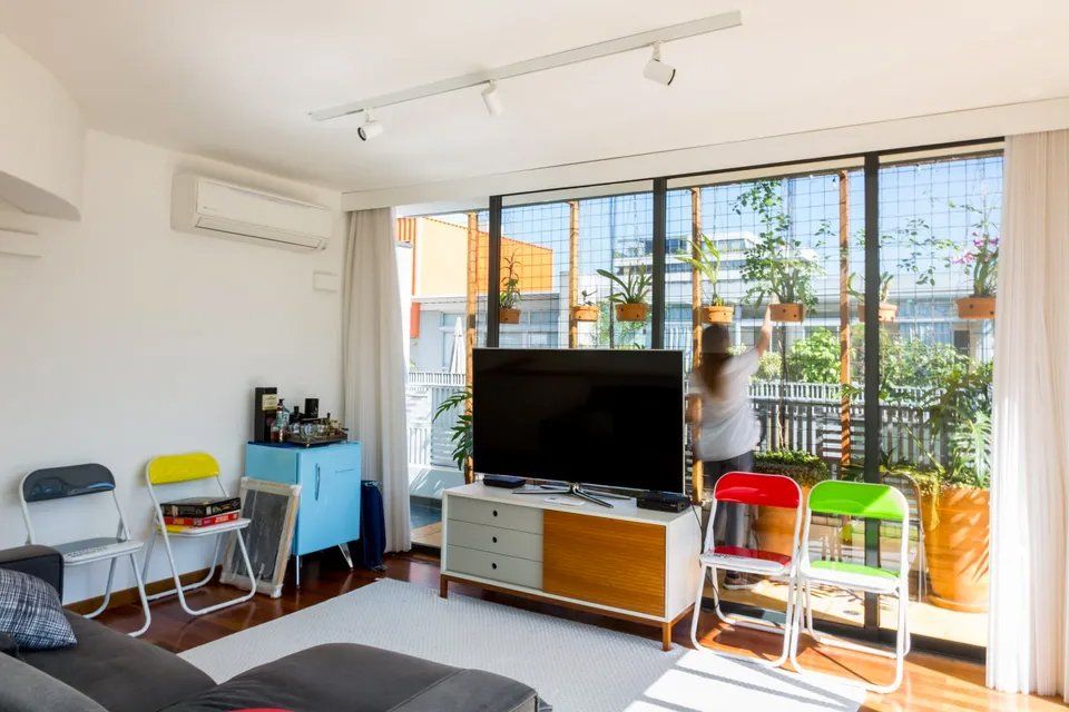 Uma sala com sofá, televisão, cadeiras e varanda.