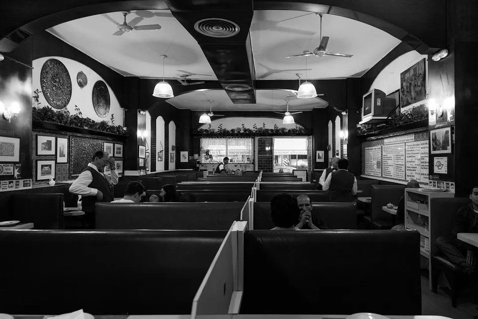 Uma foto em preto e branco de um restaurante com pessoas sentadas em mesas.