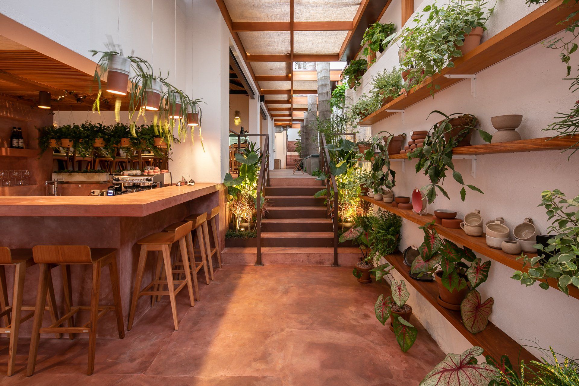 Um longo corredor com bar, bancos e prateleiras cheias de vasos de plantas.