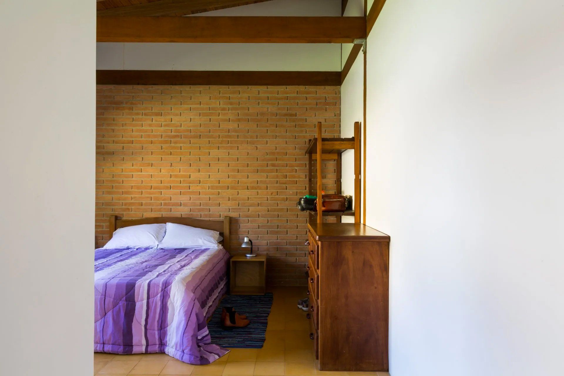 Um quarto com cama, cômoda, mesa de cabeceira e parede de madeira.