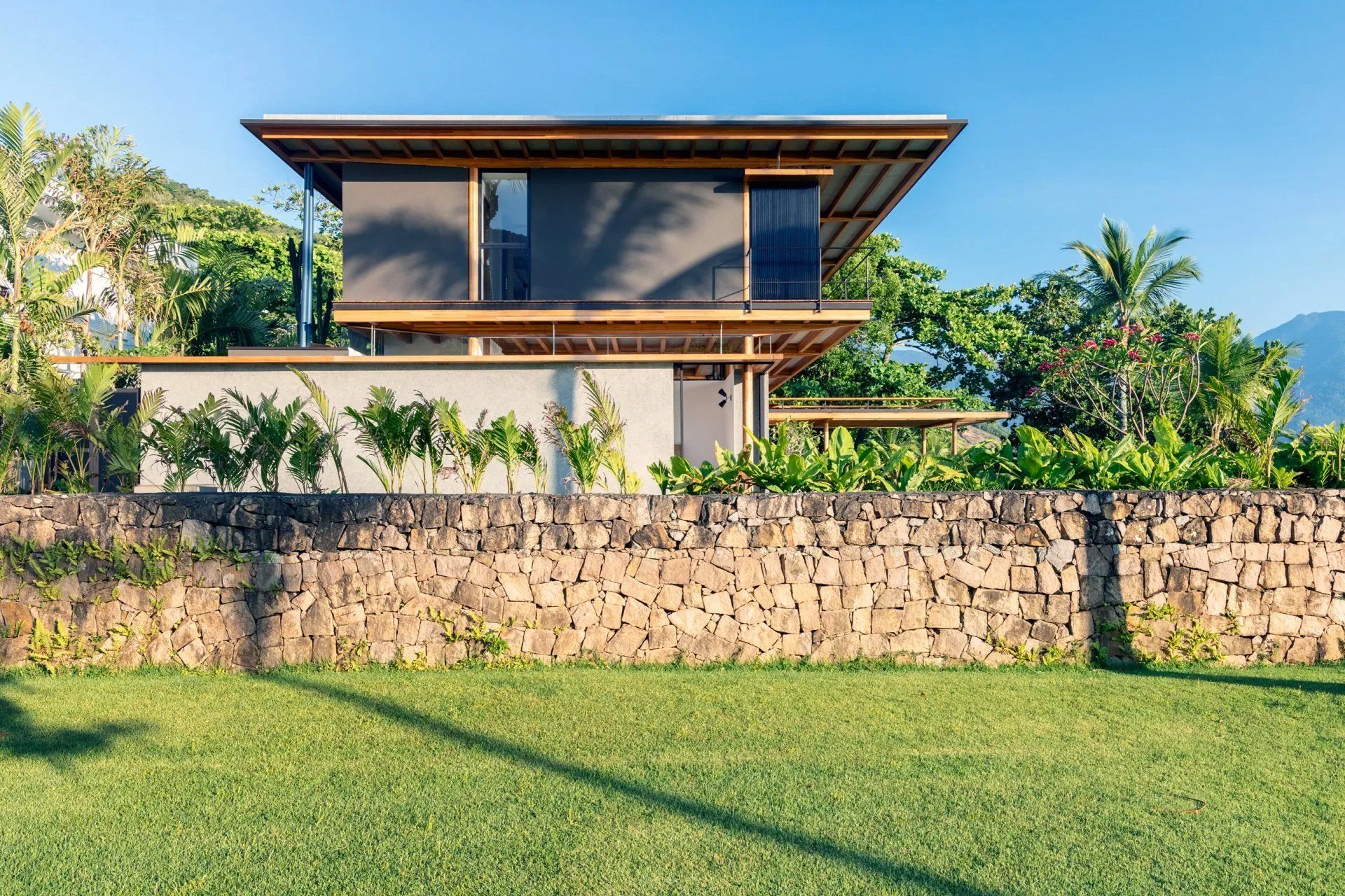 Uma casa moderna com um muro de pedra e um grande gramado na frente.