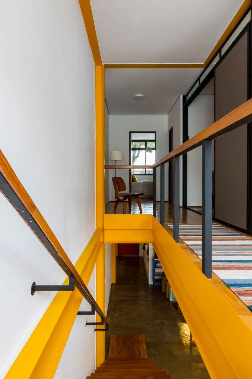 Uma escada com corrimão amarelo que leva a uma sala de estar