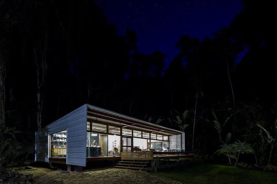 Uma pequena casa é iluminada à noite no meio de uma floresta.