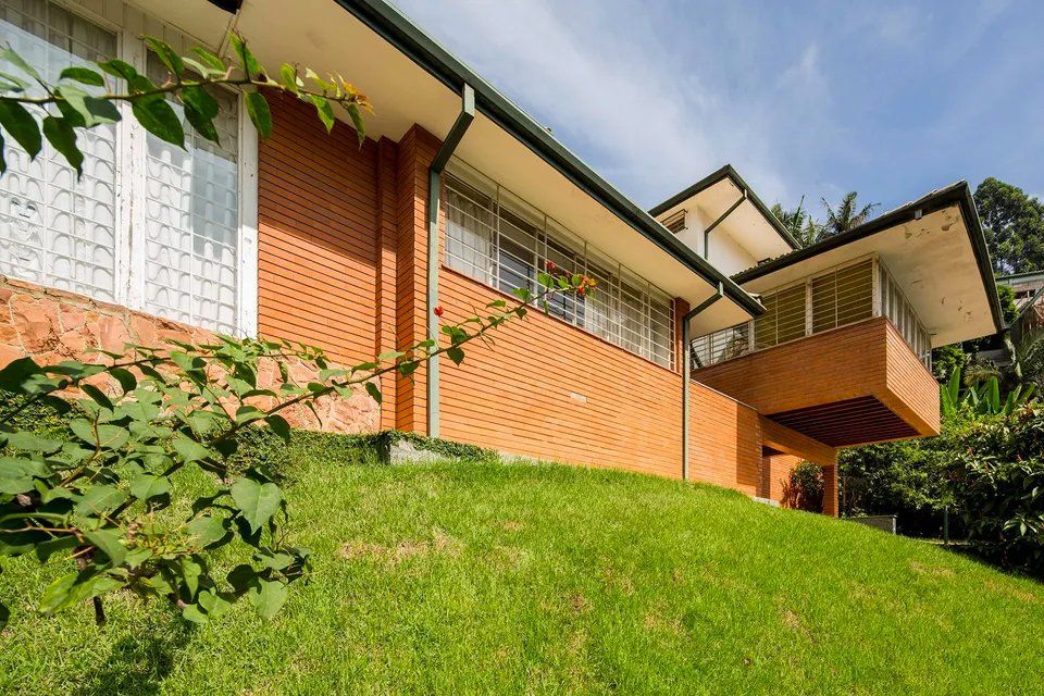 Uma grande casa de tijolos está situada no topo de uma colina gramada.