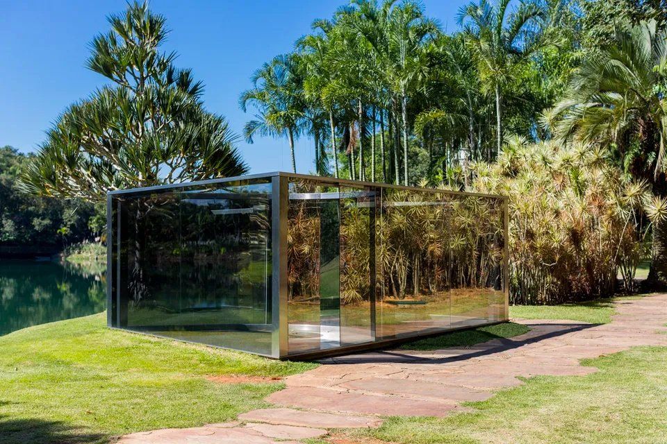 Um edifício de vidro está situado no topo de um campo verdejante próximo a um lago.