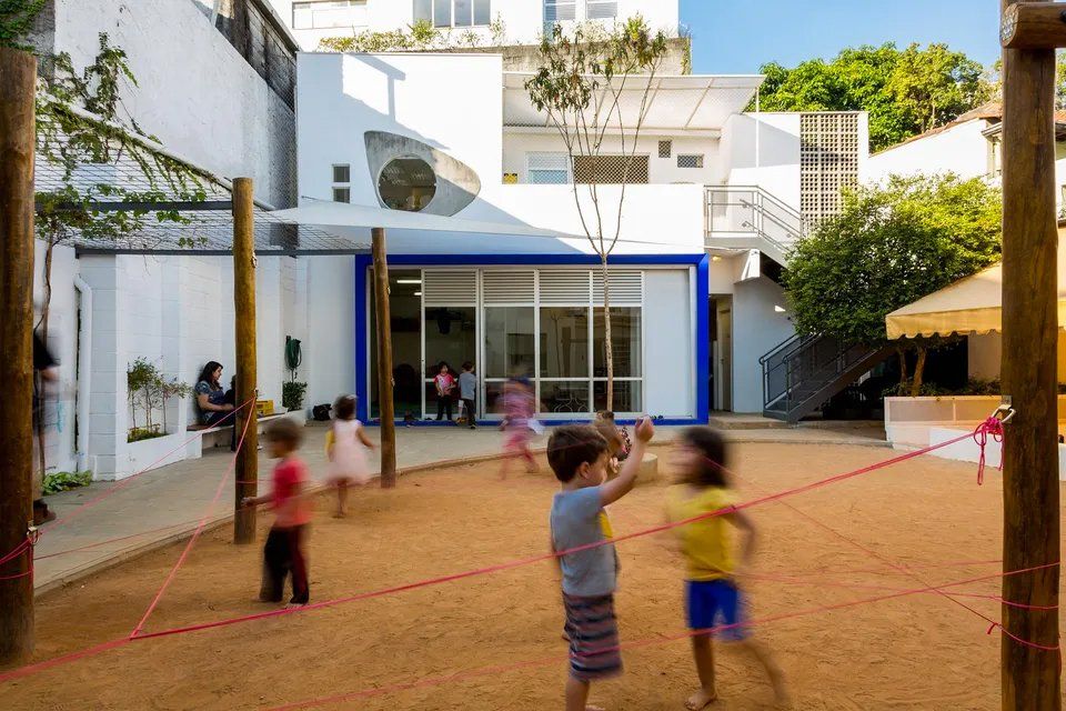Um grupo de crianças brinca em um playground em frente a um prédio.