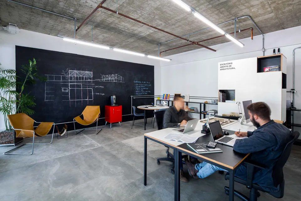 Um homem está sentado em uma mesa em um escritório usando um laptop.