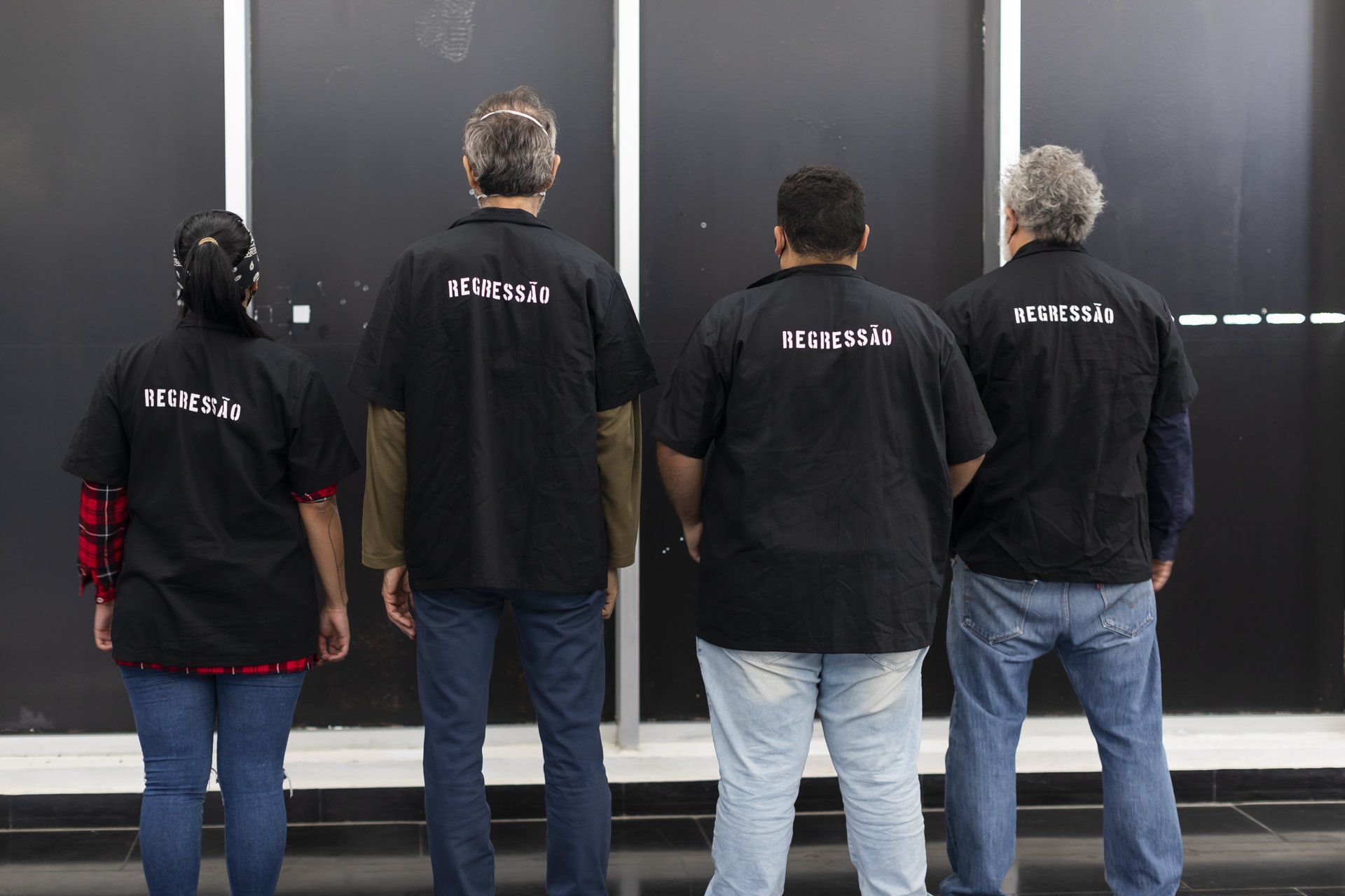 Um grupo de pessoas em frente a uma parede preta vestindo camisas pretas