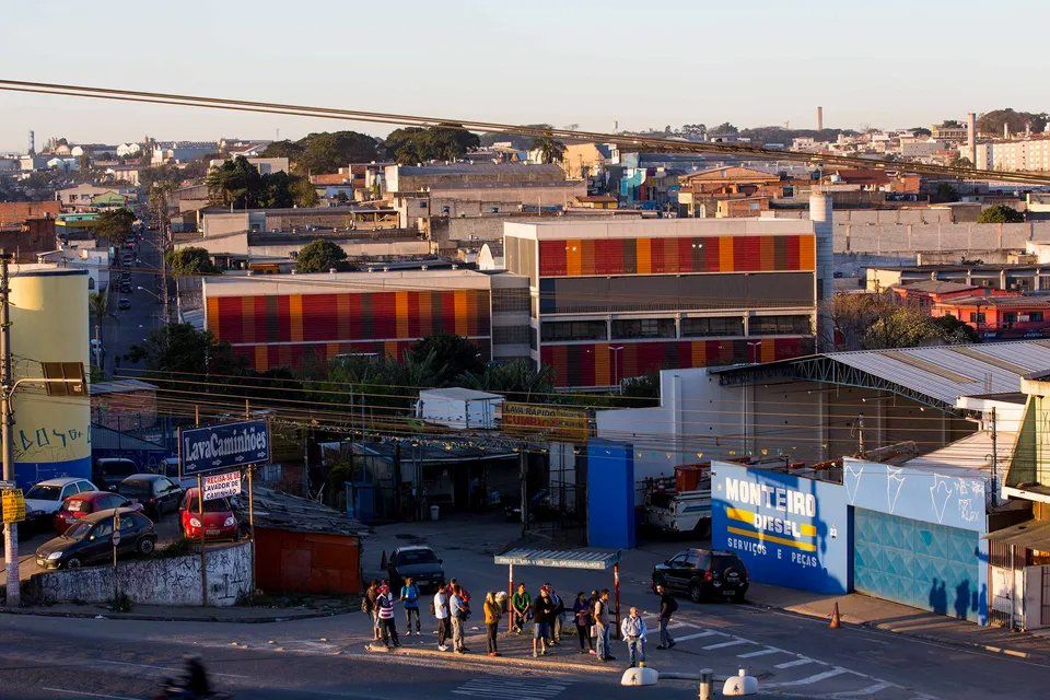 Um grupo de pessoas está parado na beira da estrada, em frente a um prédio onde está escrito 'motel'.