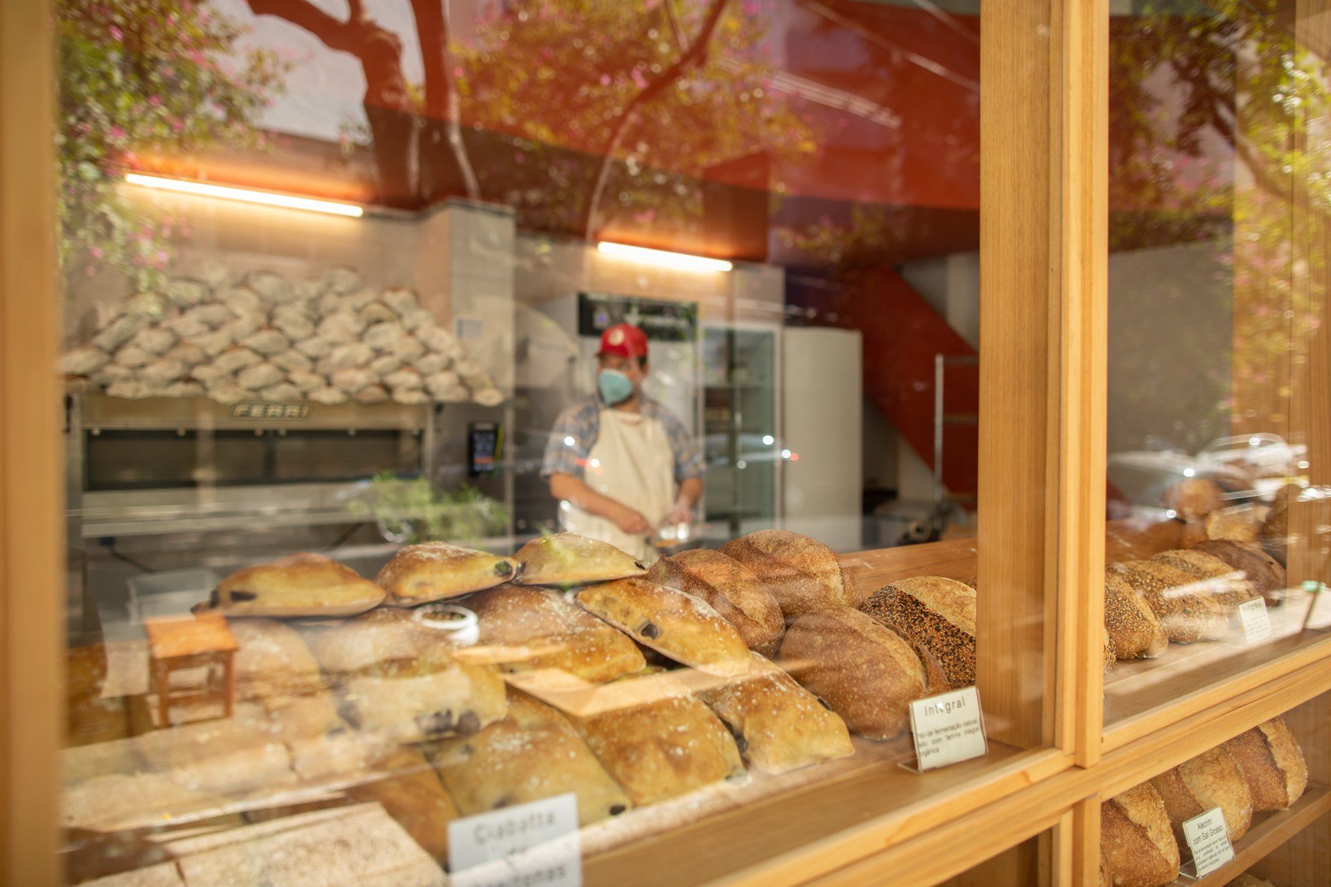 Um homem usando máscara está parado em frente à vitrine de uma padaria.
