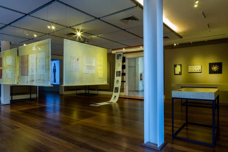 Uma sala ampla com piso de madeira e muitas pinturas na parede.