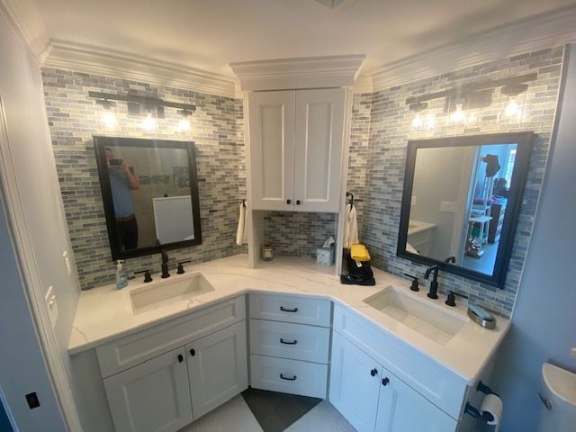 Bright bathroom vanity with two mirrors, white cabinets, and marble-style countertops under wall sconces