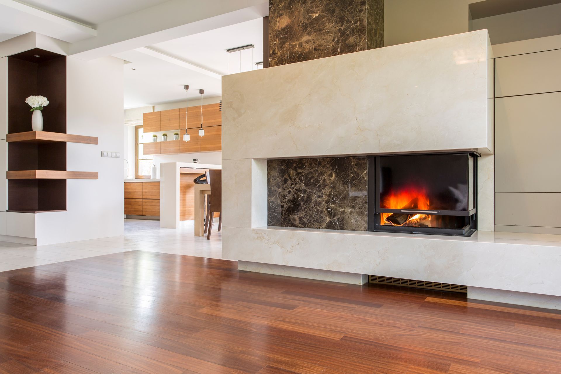 Modern living room with hardwood floors and a lit fireplace, open kitchen in the background