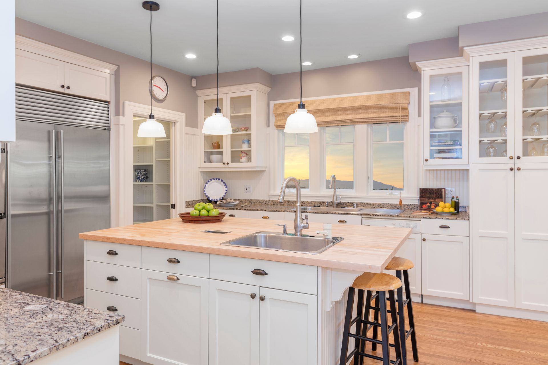Bright modern kitchen with white cabinets, stainless fridge, wood island, and pendant lights