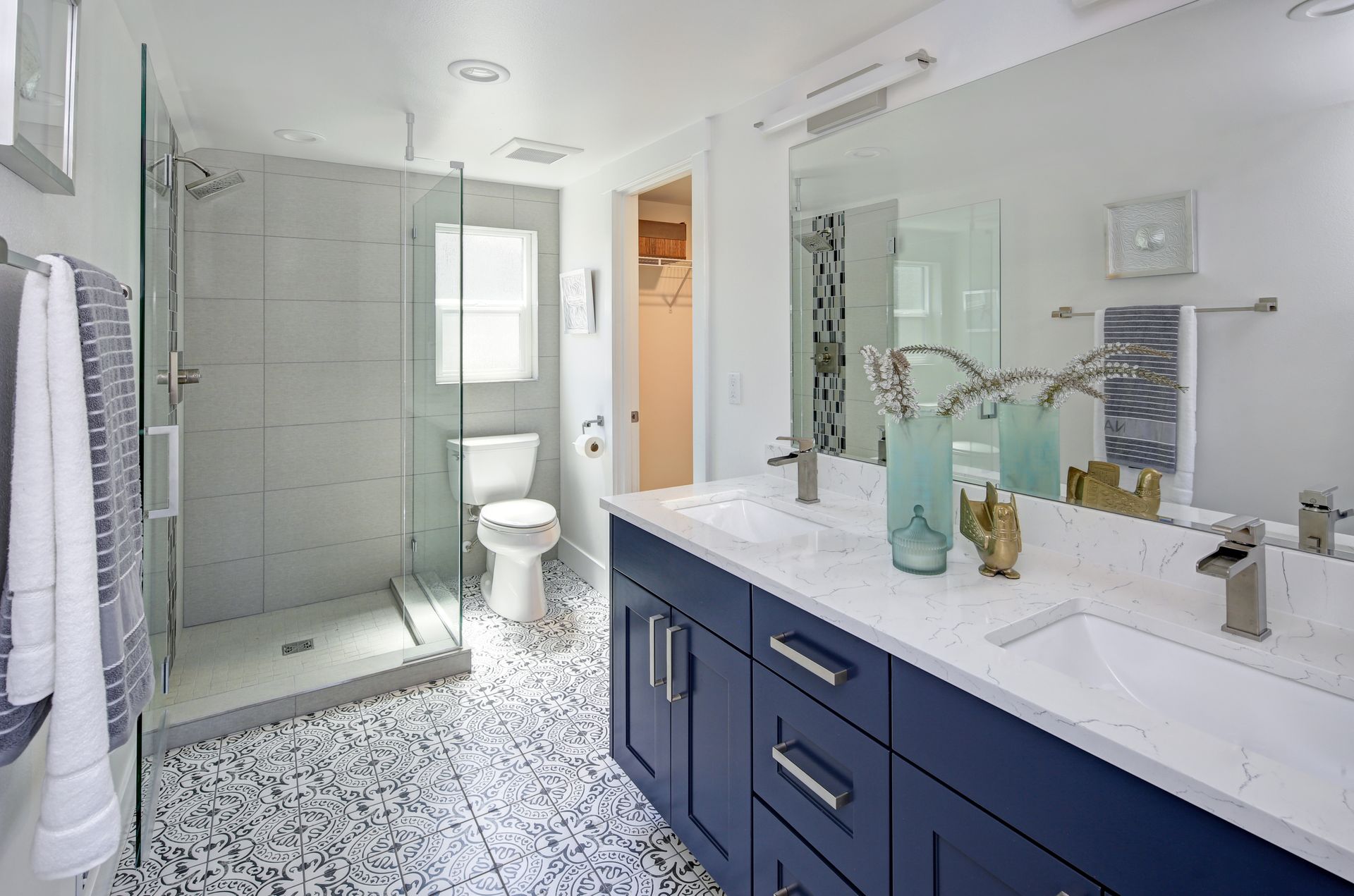 Bright bathroom with navy vanity, glass shower, white toilet, and pebble-pattern tile floor Bright bathroom with navy vanity, glass shower, white toilet, and pebble-pattern tile floor