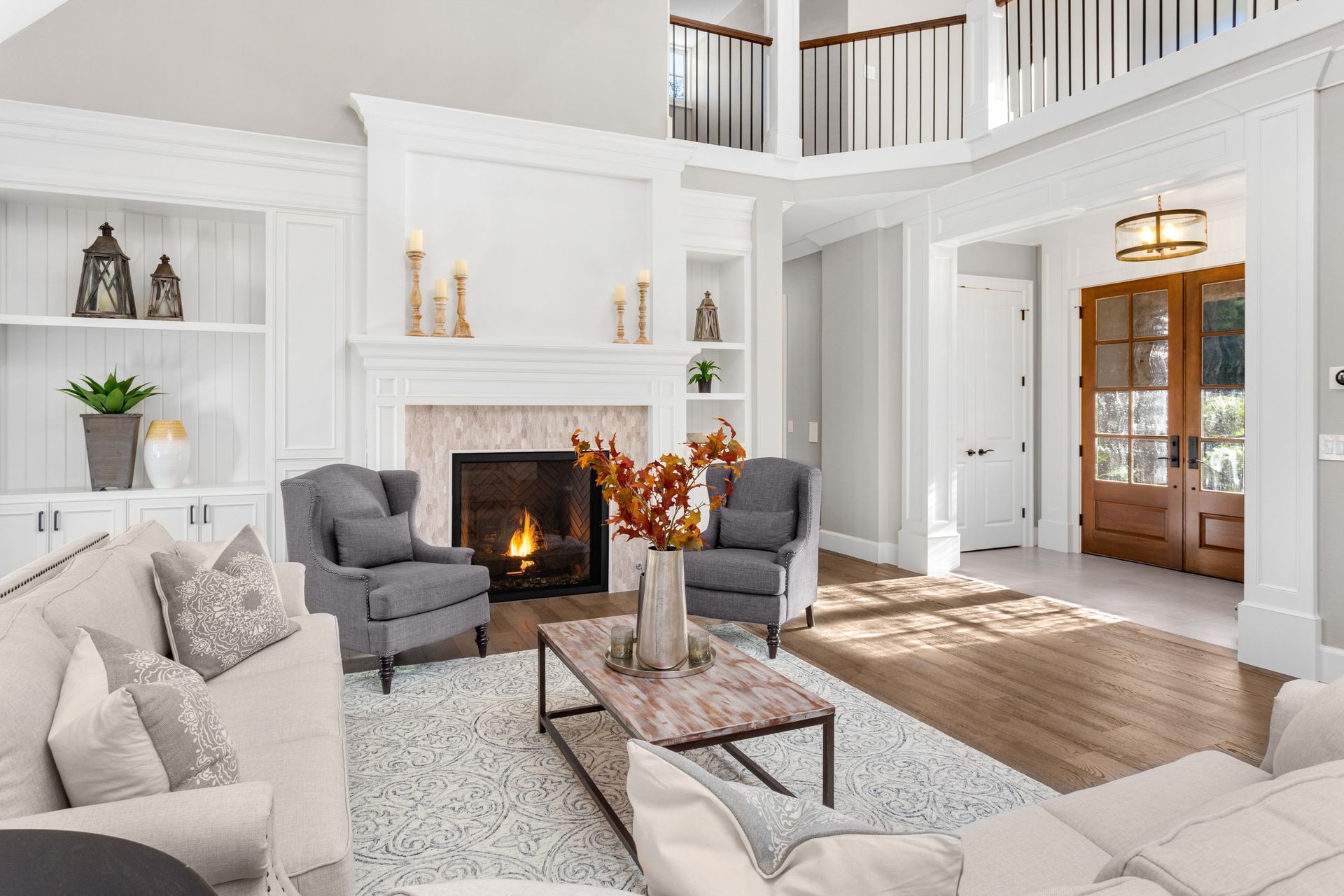Bright living room with white fireplace, gray chairs, cream sofa, and wood front door in background