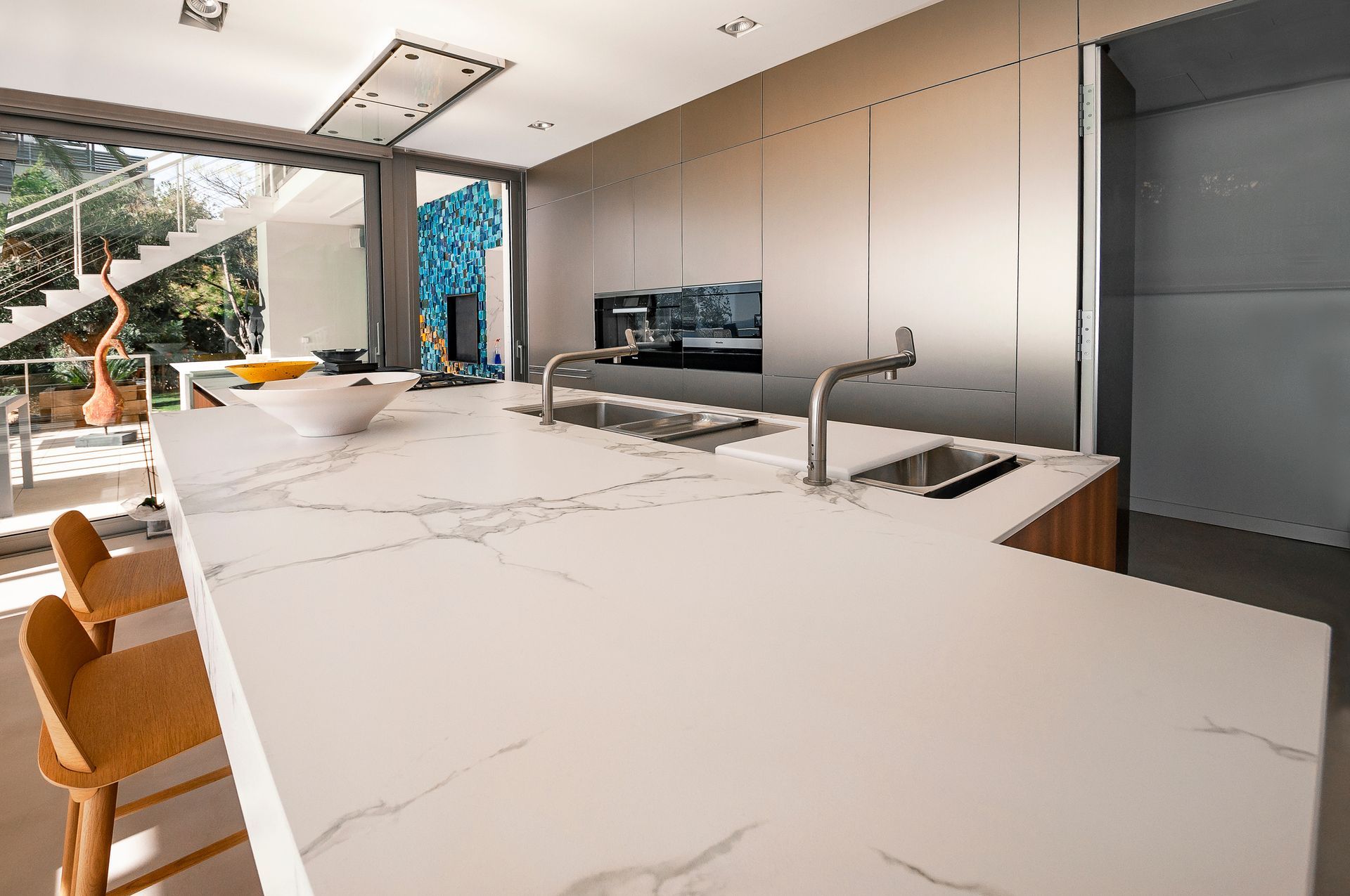 Modern kitchen with a large white island, built-in sink, black cabinets, and open view to outdoors