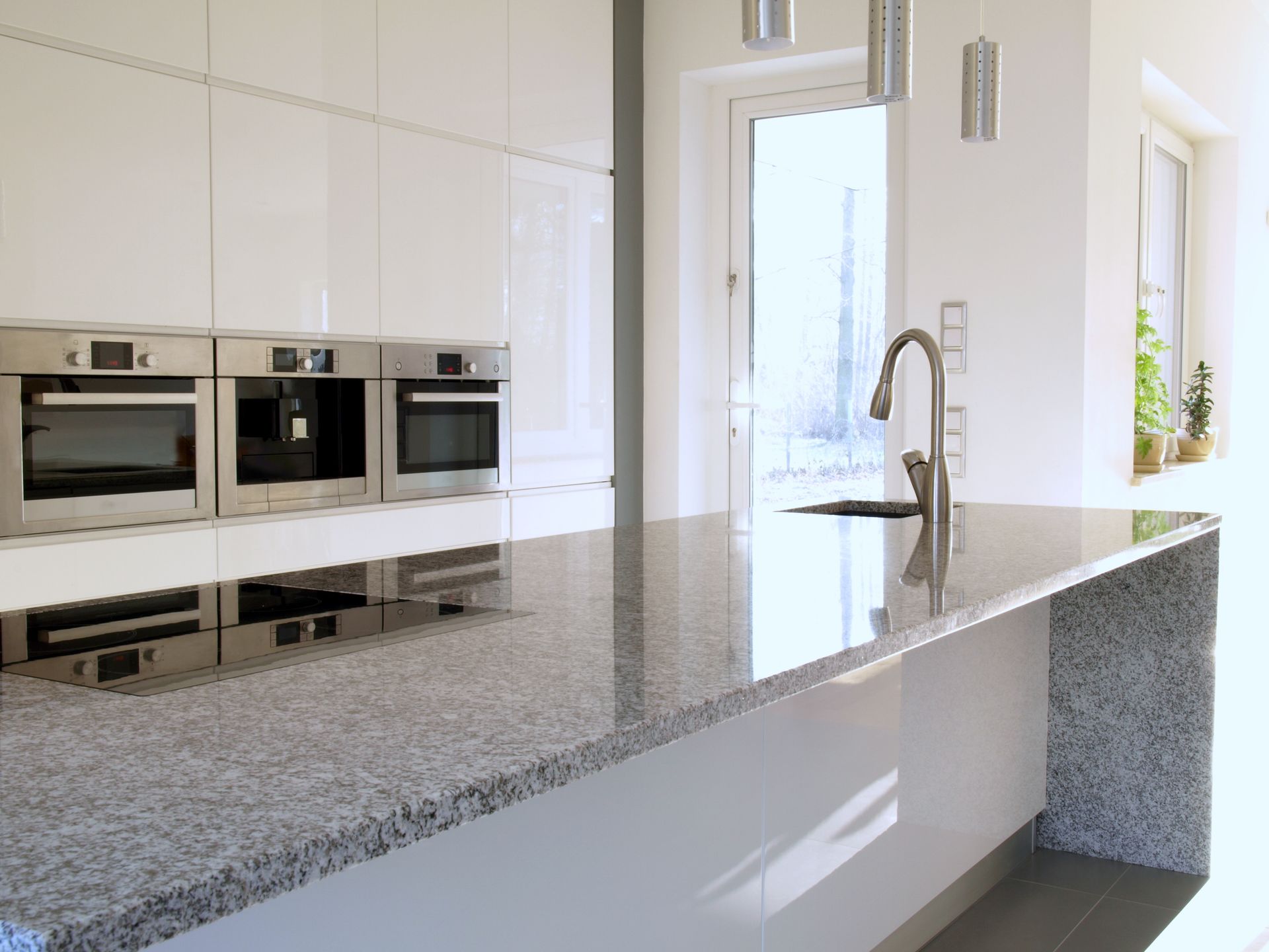 Modern kitchen with a granite island, built-in ovens, and a tall chrome faucet near bright windows Modern kitchen with a granite island, built-in ovens, and a tall chrome faucet near bright windows