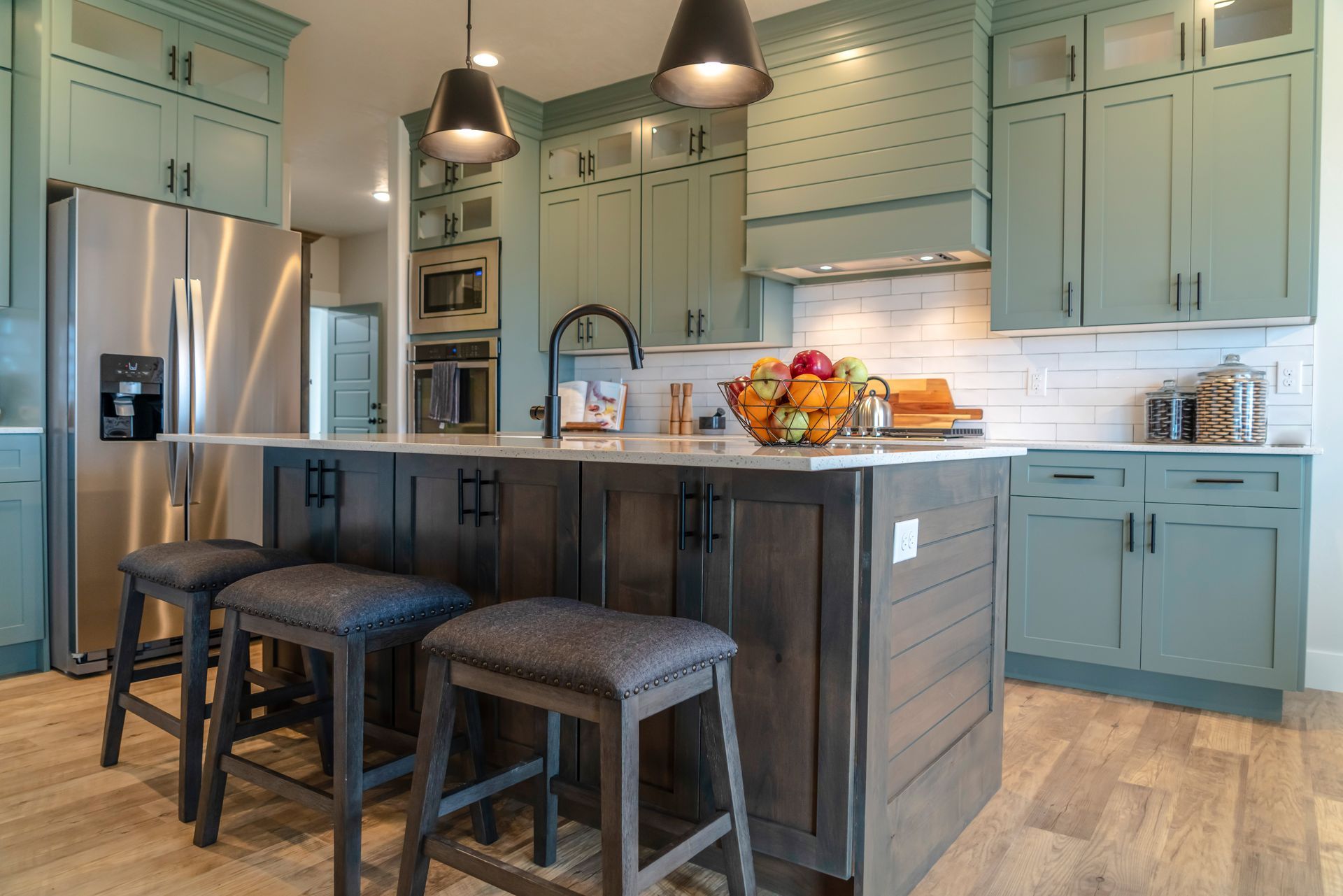 Bright kitchen with teal cabinets, stainless fridge, dark island with stools, and fruit centerpiece Bright kitchen with teal cabinets, stainless fridge, dark island with stools, and fruit centerpiece