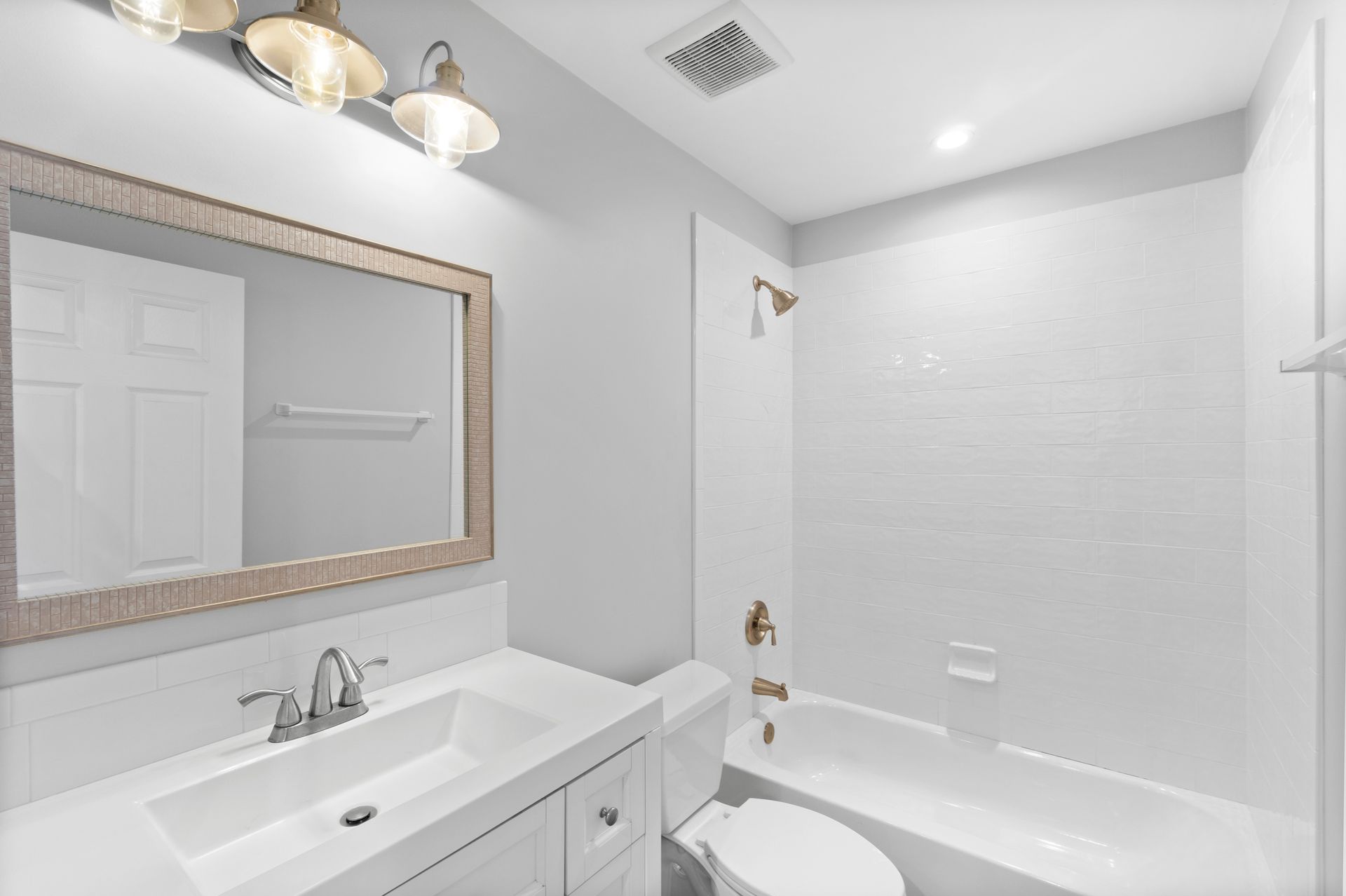 Bright white bathroom with vanity sink, mirror, lights, and shower-tub combo