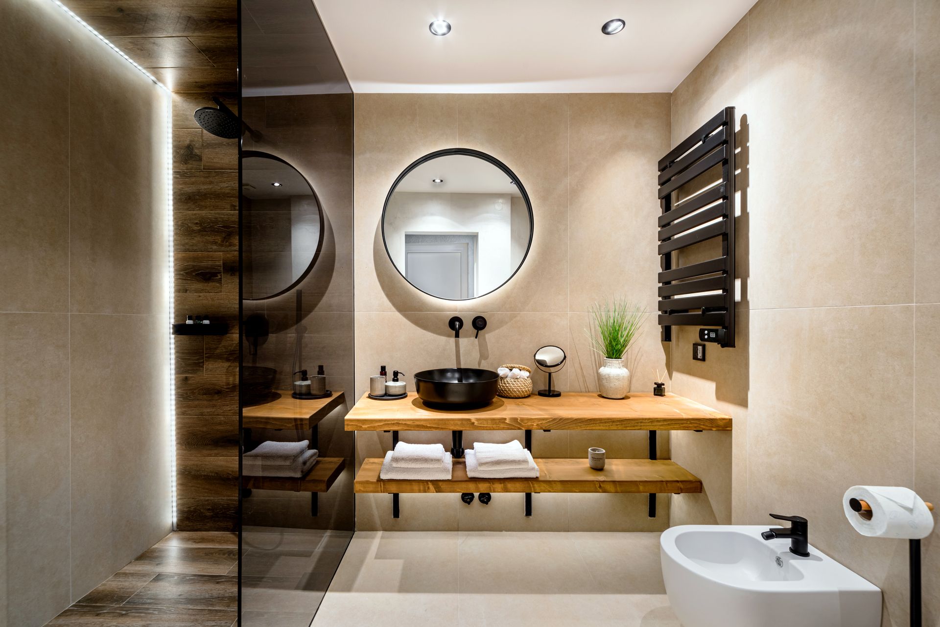 Modern bathroom with wood vanity, round mirror, sink, towel warmer, and toilet paper holder