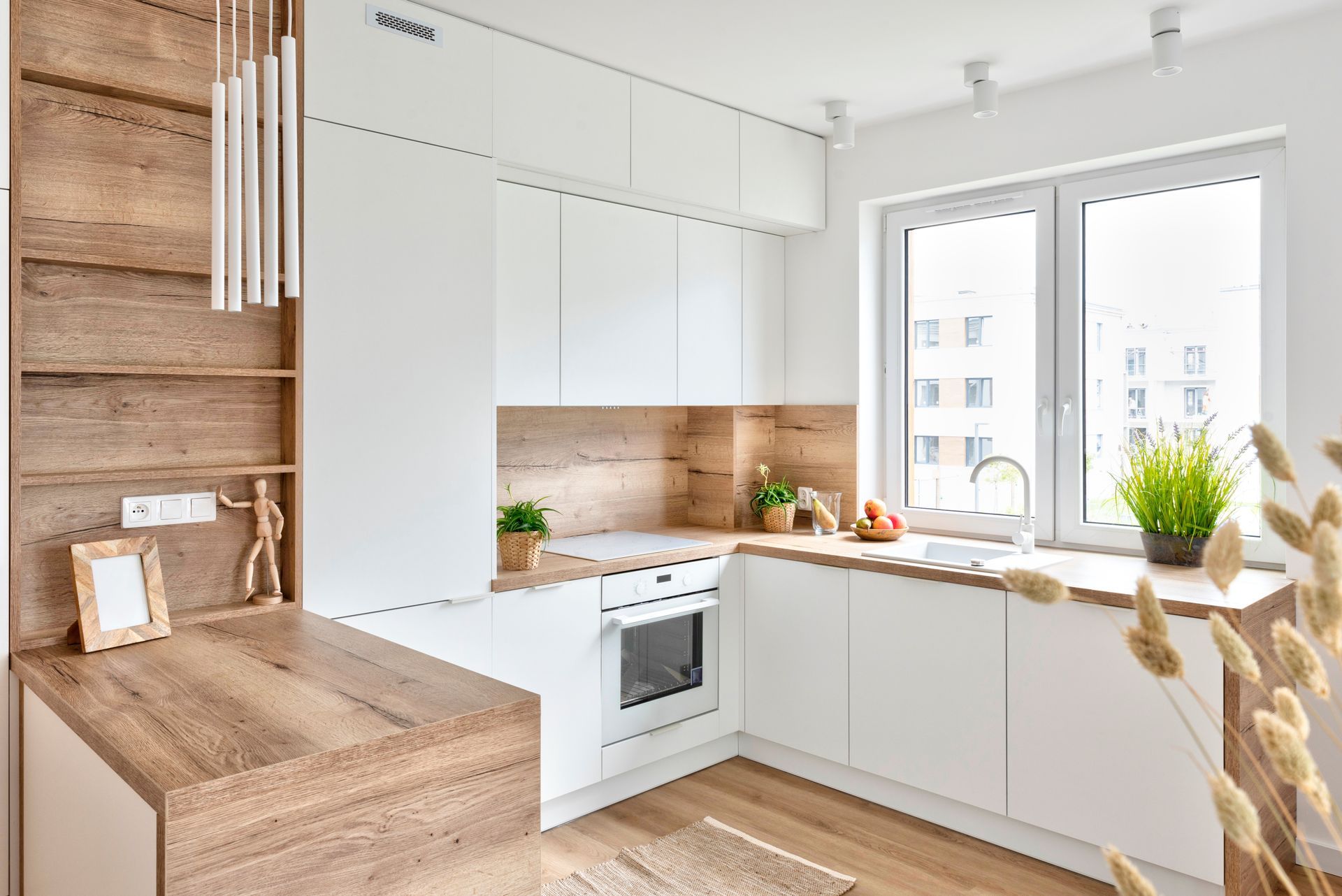 Bright modern kitchen with white cabinets, wooden accents, and large windows with city views