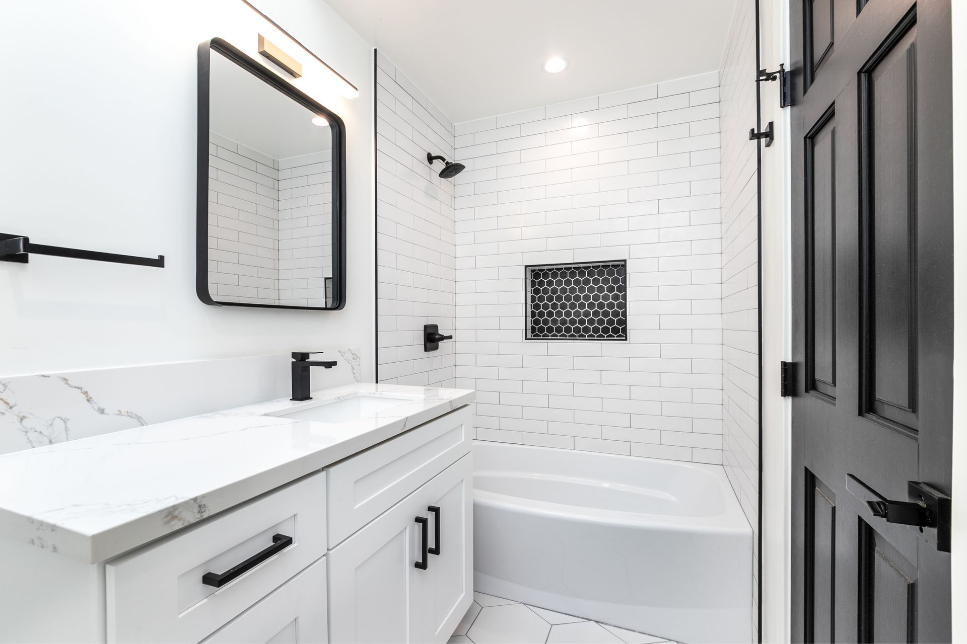 Bright white bathroom with vanity, black mirror, and tiled tub-shower area with dark door Bright white bathroom with vanity, black mirror, and tiled tub-shower area with dark door