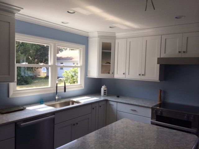 Bright white kitchen with gray cabinets, a large window over the sink, and sunlight on the countertop.