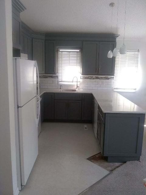 Bright kitchen with white cabinets, dark countertops, and a white refrigerator near a window.