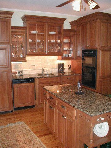 Warm kitchen with wooden cabinets, granite island, black oven, and ceiling fan.